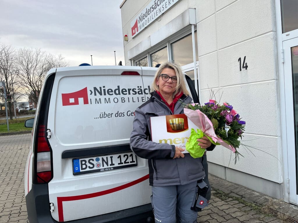Bild: © WIEDERAUFBAU Eine Kollegin der Niedersächsischen hält einen Blumenstrauß und eine Packung Merci in der Hand.