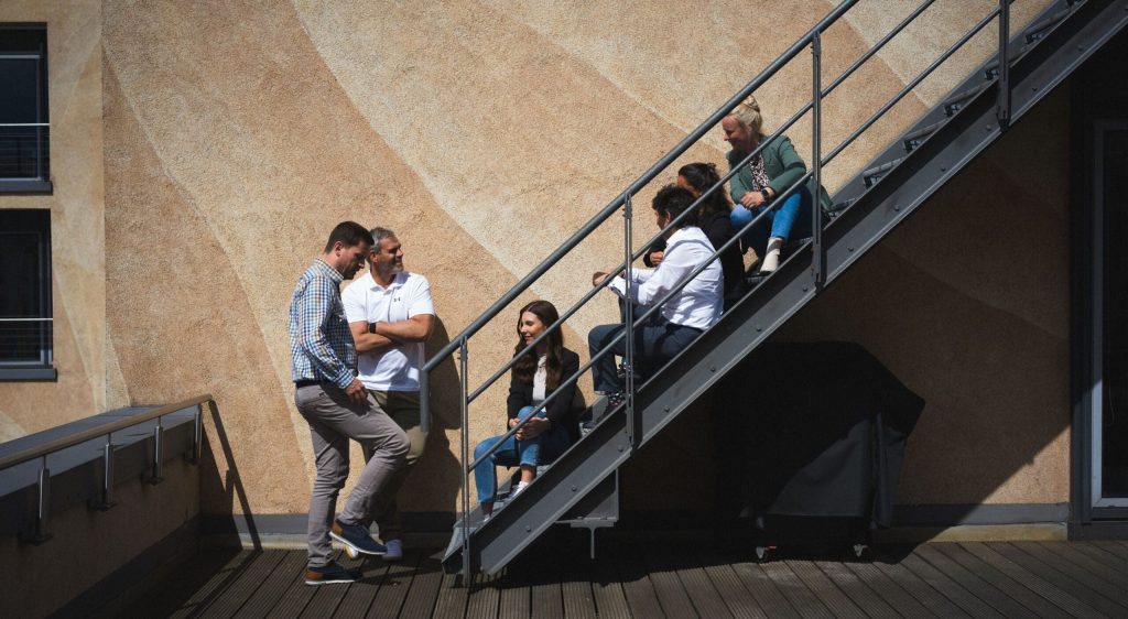 Bild: © Tom Tautz Mitarbeitende der WIEDERAUFBAU sitzen in gemütlicher Runde auf der Treppe der Dachterrasse.