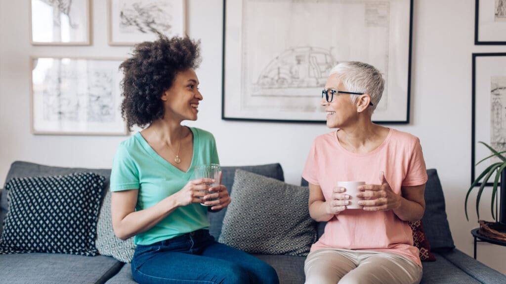 © iStockphoto.com/MixMedia Zwei Frauen sitzen auf einem Sofa und lächeln sich an.
