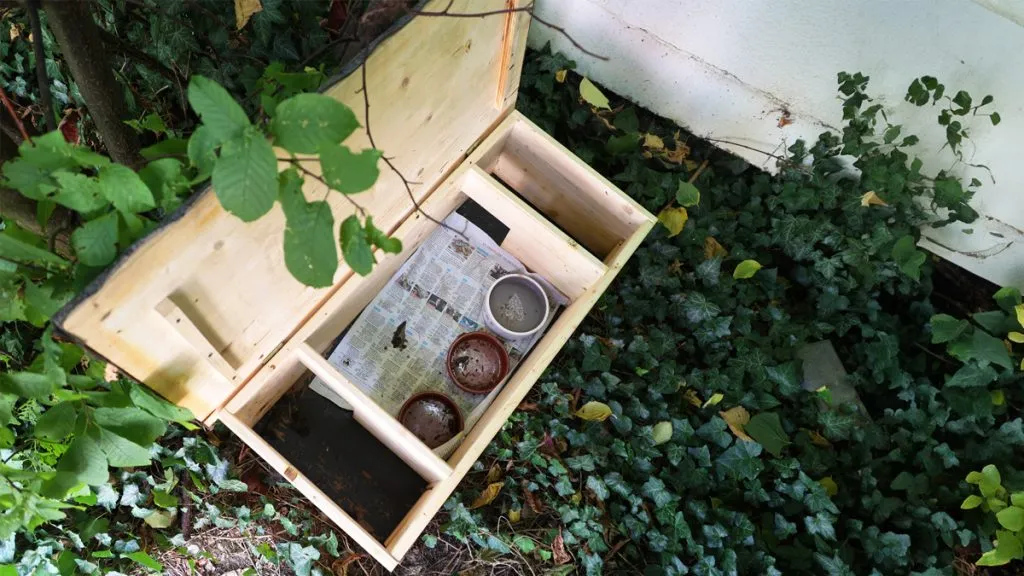 Bild: © WIEDERAUFBAU Ein Igel-Futterhaus steht in einem geschützten Bereich, der Deckel ist aufgeklappt.