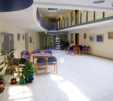 Bild: © WIEDERAUFBAU Das Foyer des Betreuten Wohnen Braunschweig-Weststadt mit ein paar Pflanzen im Vordergrund und zwei Sitzgruppen im Hintergrund.