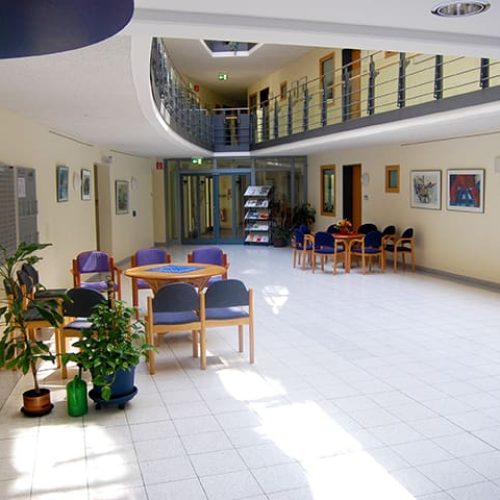 Bild: © WIEDERAUFBAU Das Foyer des Betreuten Wohnen Braunschweig-Weststadt mit ein paar Pflanzen im Vordergrund und zwei Sitzgruppen im Hintergrund.