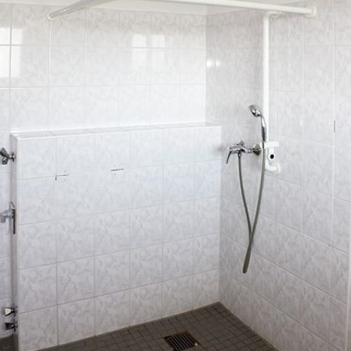 Bild: © WEDERAUFBAU Beispielhaft eine begehbare Dusche mit grauen Fließen und Durschvorhangvorrichtung.