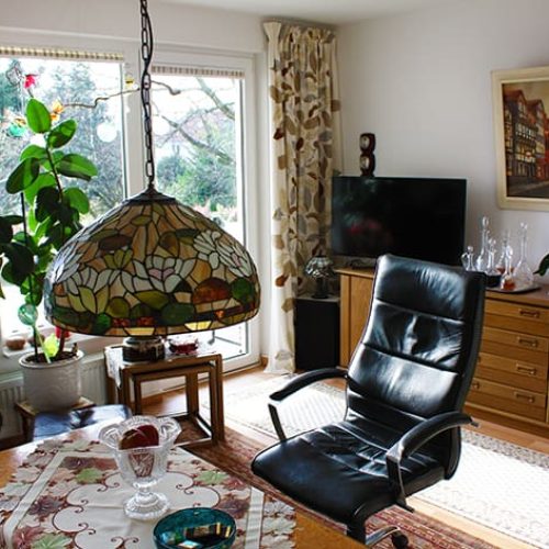 Bild: © WIEDERAUFBAU Beispiel eines Wohnzimmers mit großen Fenster, Balkon und hellbraunen Bodenbelage im Betreuten Wohnen Querum.