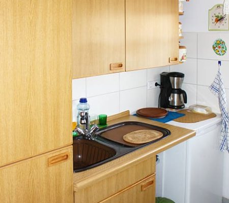 Bild: © WIEDERAUFBAU Beispiel Küche mit weißen Fliesenspiegel und grauen Bodenfliesen im Betreuten Wohnen Queurm.