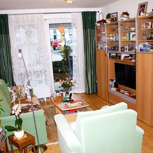 Bild: © WIEDERAUFBAU Beispiel eines Wohnzimmers mit Terrasse und hellbraunen Bodenbelag im Betreuten Wohnen Volkmarode.